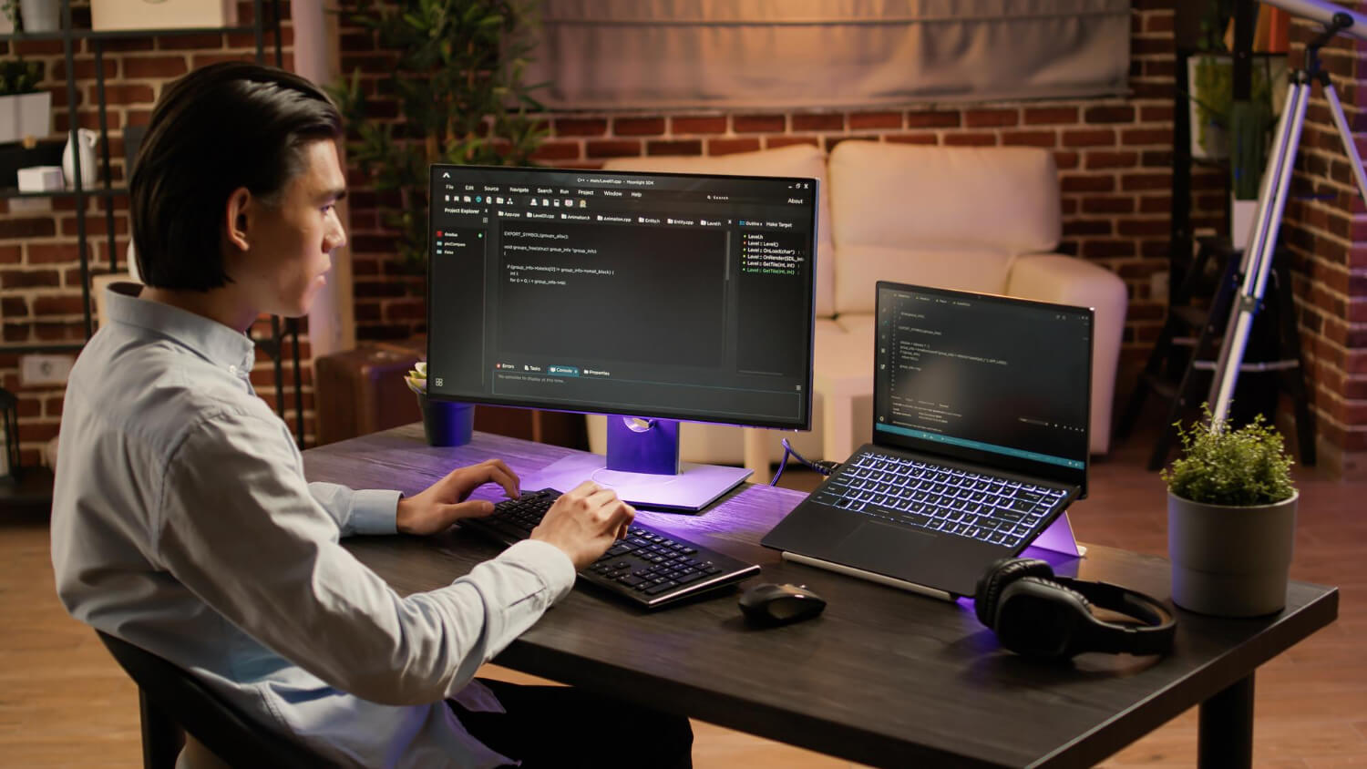 Persona programando en una computadora portatil y monitor en un escritorio moderno