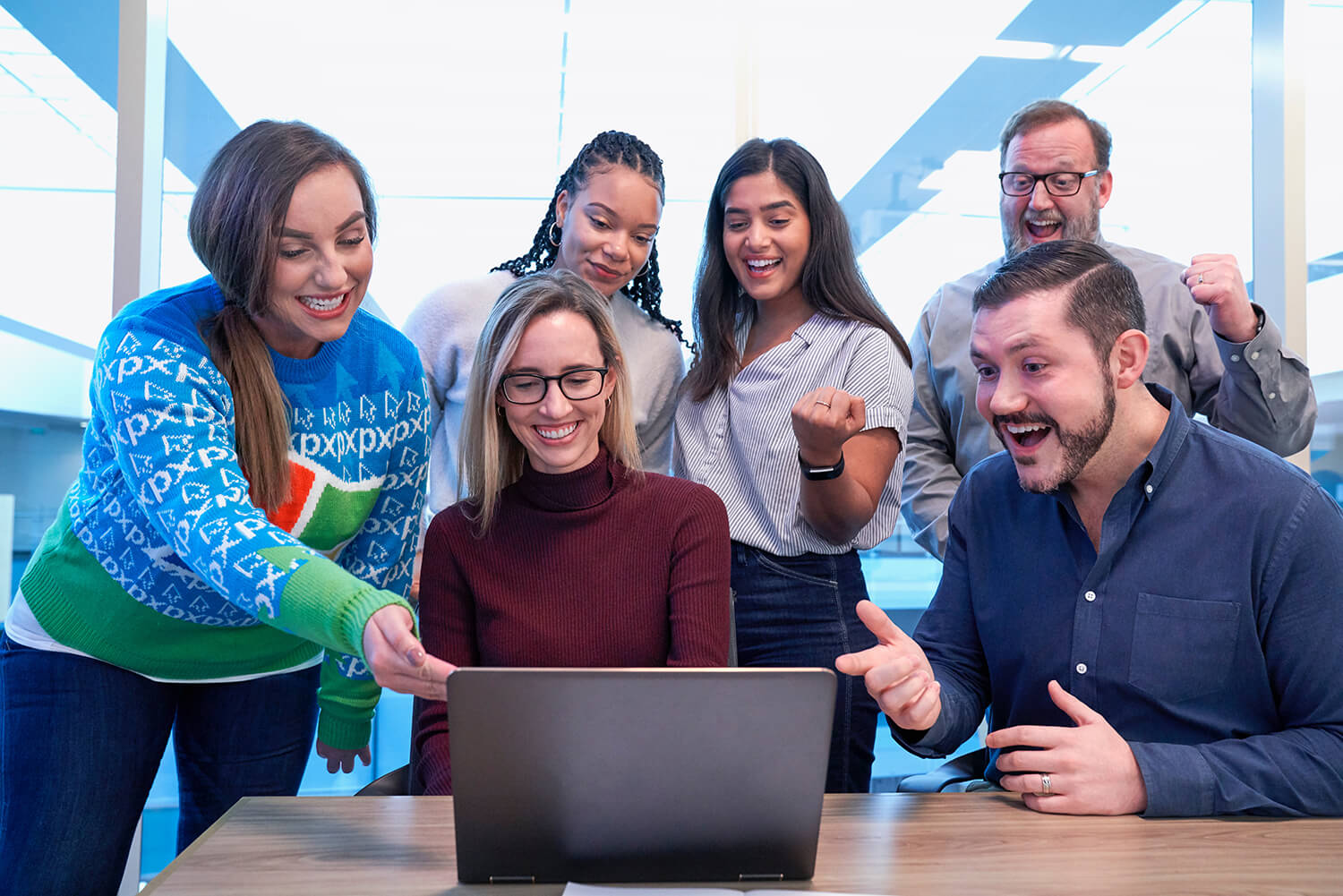 Personas reunidas alrededor de una laptop, sonrientes y entusiastas.