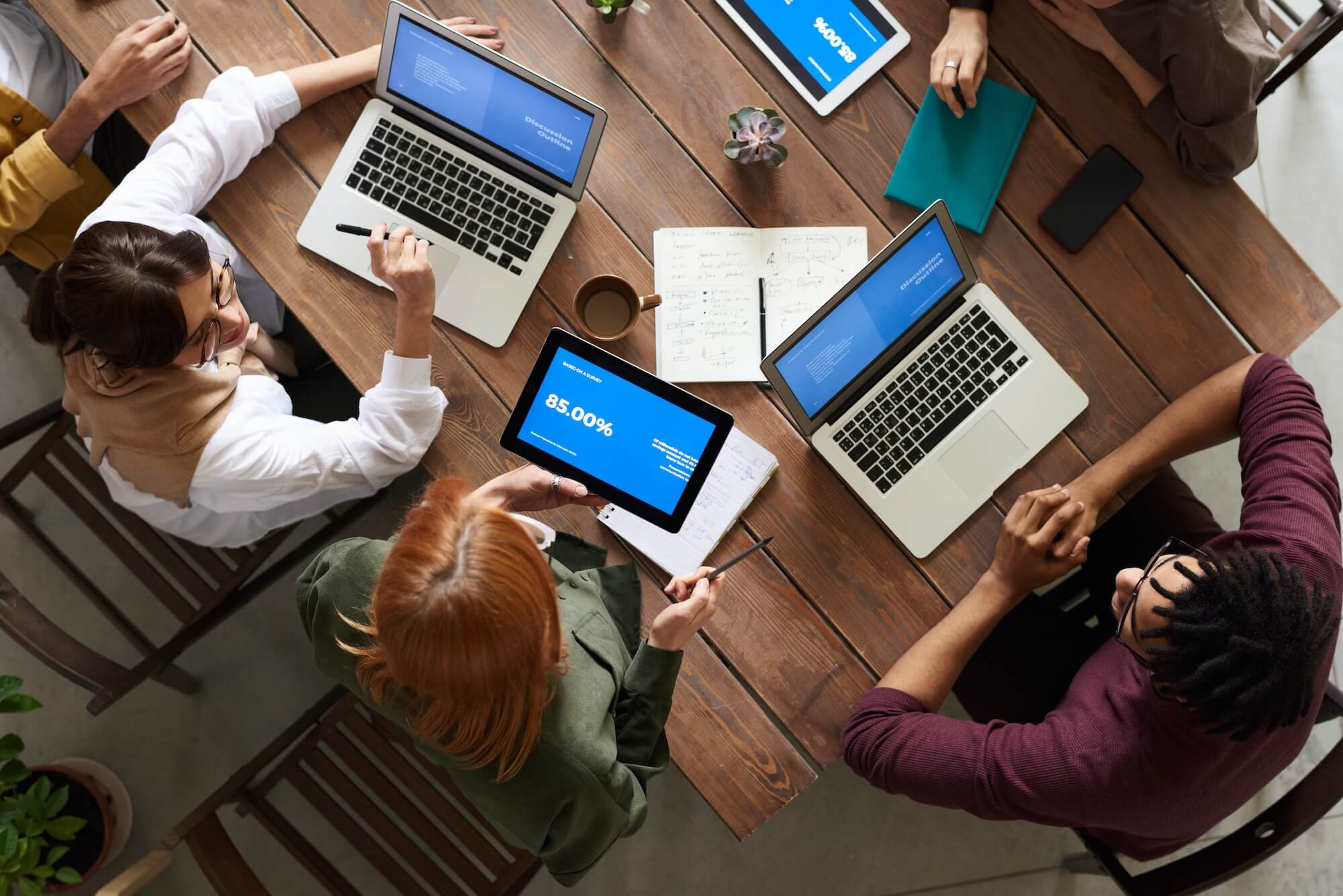 Personas reunidas en mesa con portátiles y tabletas.