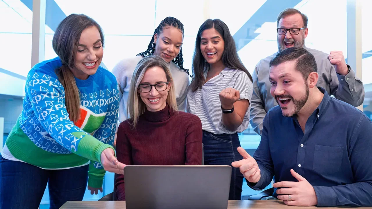 Personas reunidas alrededor de una laptop, sonrientes y entusiastas.