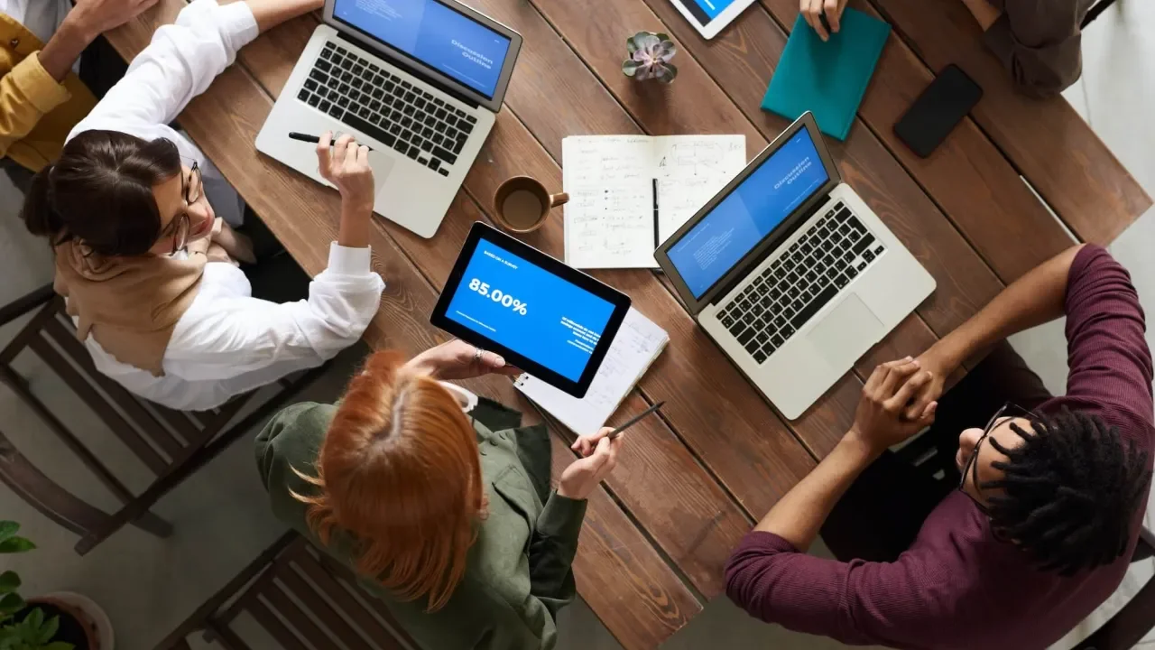 Personas reunidas en mesa con portátiles y tabletas.