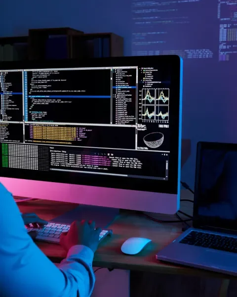 Programador trabajando en una computadora, pantalla con código. Ambiente oscuro, lucecitas coloridas