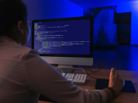 Persona programando en una computadora en una sala iluminada en azul