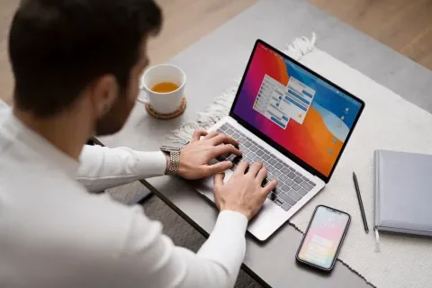Persona trabajando en una laptop con taza de té y móvil en una mesa