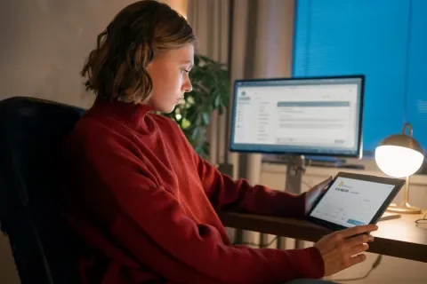 Persona concentrada usando una tableta y computadora en un escritorio iluminado