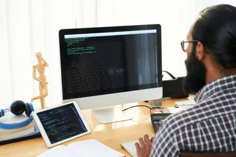 Persona programando en una computadora, con una tablet al lado.